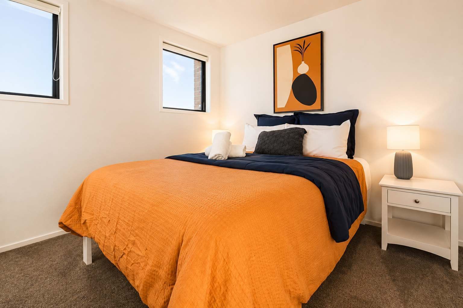 Un dormitorio con cama, mesita de noche, lámpara y un cuadro en la pared.