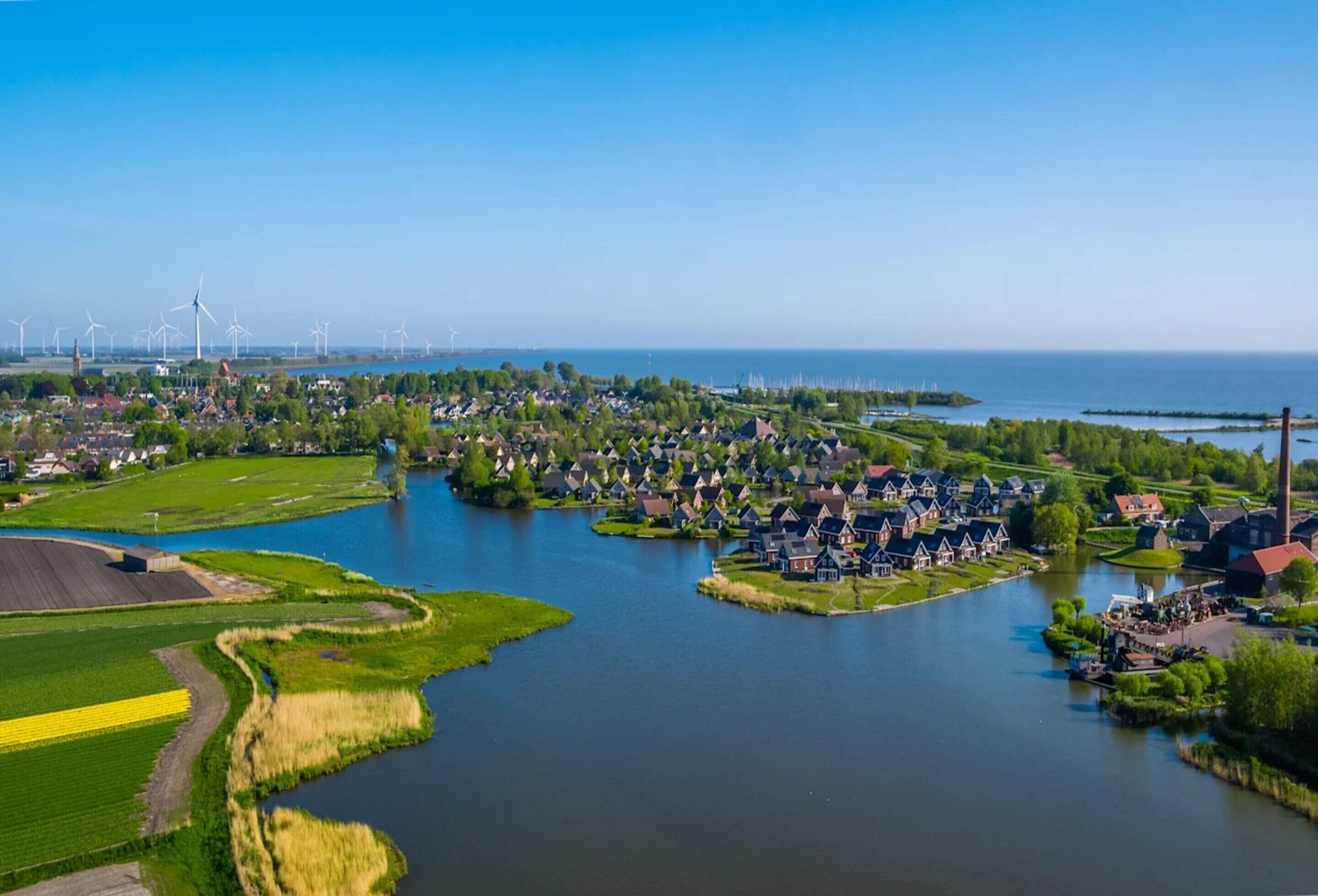 A riverside town with houses, a dock, and wind turbines in the background.