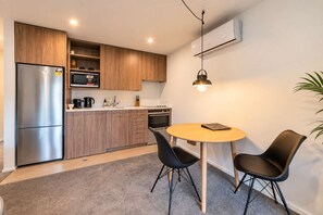 A modern kitchen with a refrigerator, microwave, and stove, a round wooden table with two chairs, and a hanging pendant light.