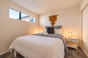 A bedroom with a bed, bedside lamps, a window, and a wall-mounted macrame piece.