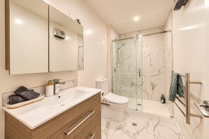 Un baño moderno con un espejo grande, un lavamanos blanco, un inodoro y una ducha con mampara de vidrio.