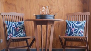 Twee houten stoelen met bloemenkussens, een klein rond tafeltje, en een metalen pot met glaswerk op tafel.