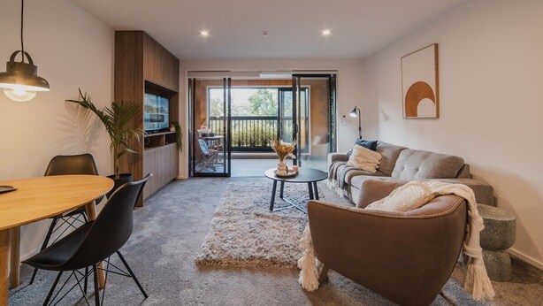 Een moderne woonkamer met een bank, een eettafel en stoelen. Er is een balkon met uitzicht op het landschap.