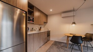 Een compacte keuken met een inbouwkoelkast, houten kastjes, een kleine eettafel met twee stoelen, en een hanglamp.