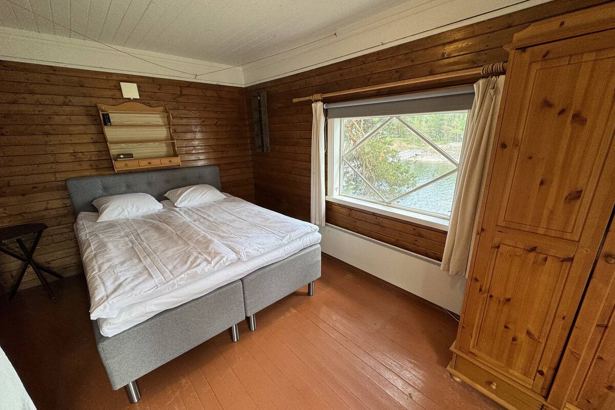 Une chambre à coucher avec un lit, des murs en bois, une fenêtre donnant sur un beau paysage et une armoire.