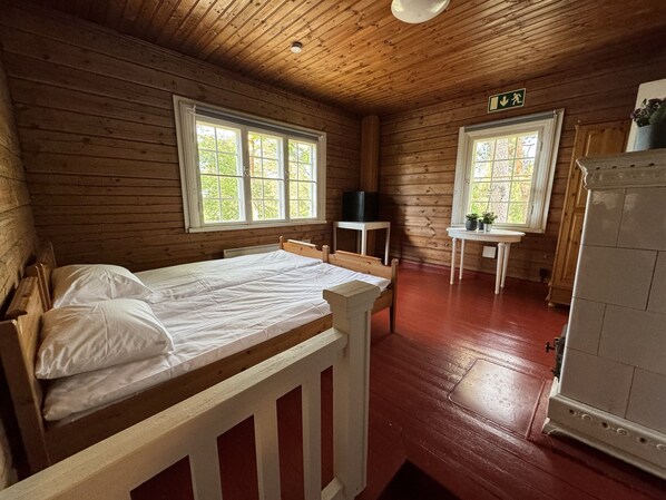 Una habitación de cabaña de madera con una cama, dos ventanas, una mesita y un refrigerador.