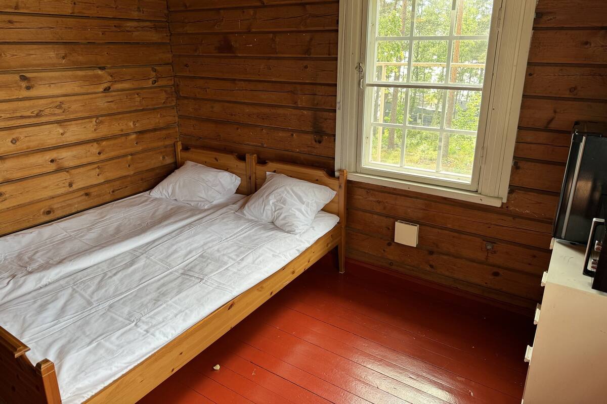 Un lit simple dans une chambre de cabane en bois avec une fenêtre.
