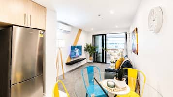 A compact living space with a kitchenette, a flat-screen TV, a dining area with a table and chairs, and a view through a sliding glass door.