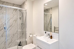 A modern bathroom with a glass-enclosed shower, a white sink, and a large mirror. - Designer CBD Stay | 2BR + Parking | Sleeps 5 (Christchurch Central City)