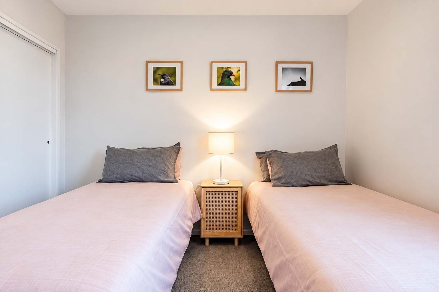 A bedroom with two beds, a bedside table with a lamp, and three framed pictures on the wall.
