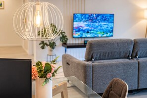 A modern living room with a grey sofa, a glass coffee table, a decorative plant, and a television mounted on the wall.