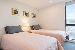 A hotel room with two beds, a nightstand with a lamp, and three framed pictures on the wall.