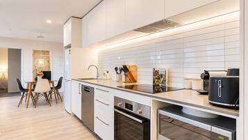 Una cocina moderna con armarios blancos, horno empotrado y cafetera.