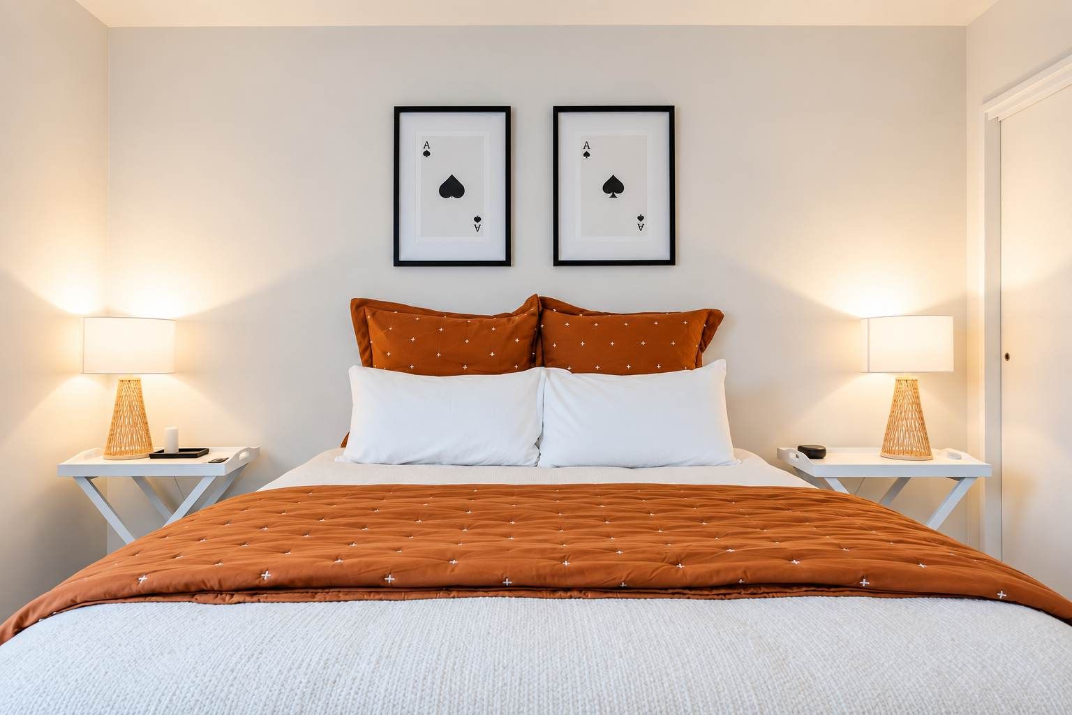 A bedroom with a bed, two nightstands, two lamps, and two framed playing cards on the wall.