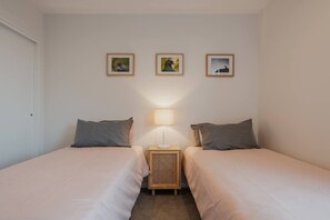 Una habitación con dos camas, una mesita de noche con lámpara y tres cuadros en la pared.
