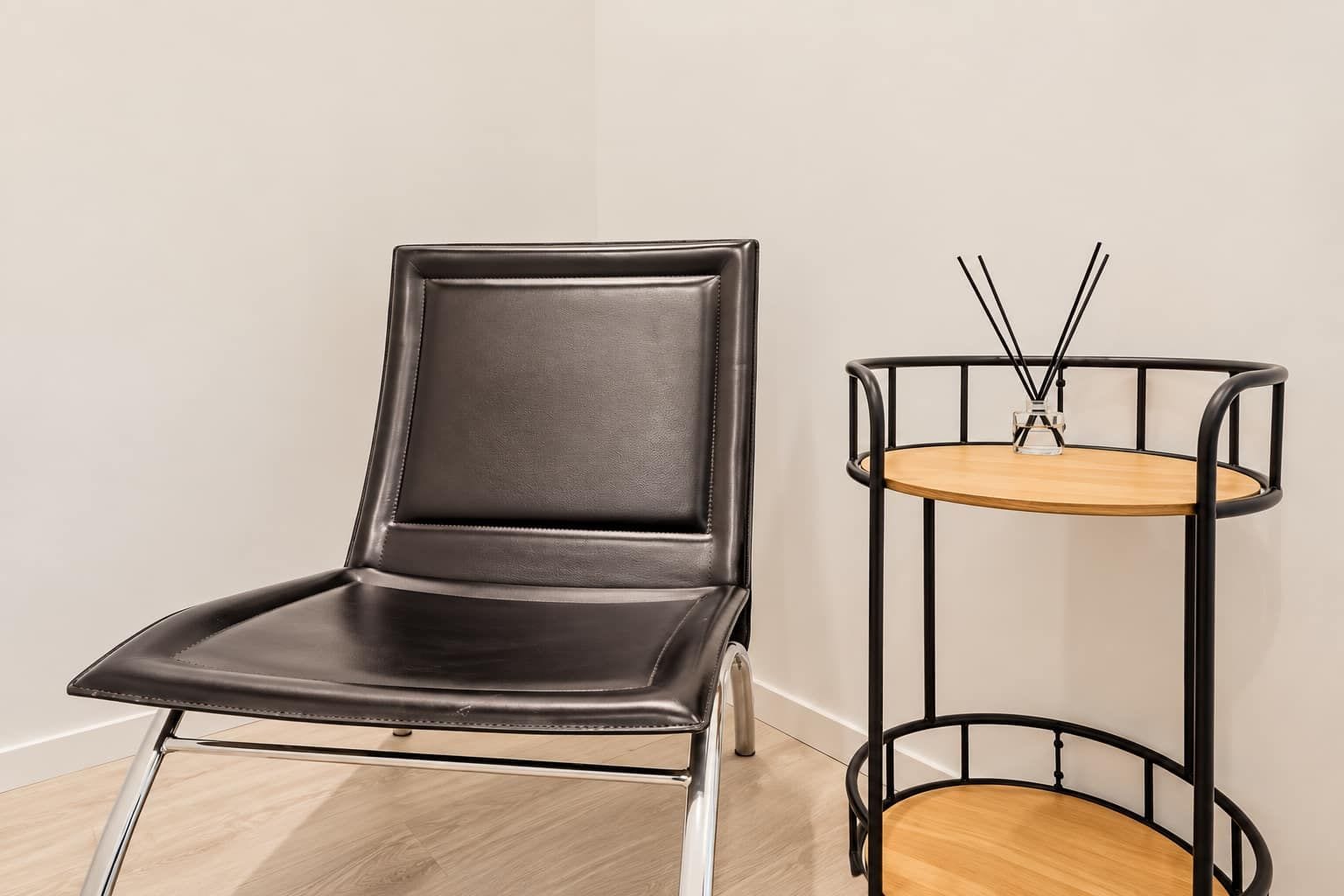 A black leather chair with a metal frame and a round wooden table with a metal frame and a glass object on top.
