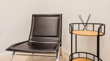 A black leather chair with a metal frame and a round wooden table with a metal frame and a glass object on top.