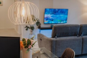 Una sala de estar moderna con un sofá gris, un televisor en la pared y una lámpara colgante.
