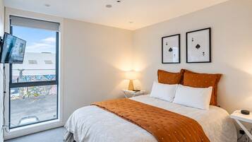 A hotel room with a bed, a TV, a window with a view of graffiti, and two framed playing cards on the wall.