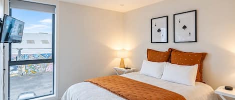A hotel room with a bed, a TV, a window with a view of graffiti, and two framed playing cards on the wall.