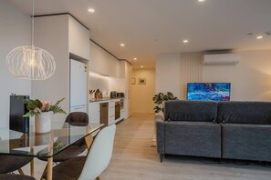 Una sala de estar moderna con un sofá gris, una mesa de comedor de vidrio y una cocina al fondo.