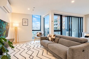 Un salon moderne avec un canapé, un fauteuil, une lampe sur pied et une grande fenêtre donnant sur des immeubles.