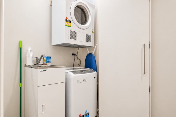 A laundry area with a front-loading washer and dryer, a green mop, and a bottle of detergent.