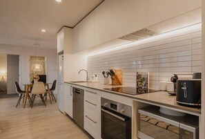 Una cocina moderna con armarios blancos, horno integrado y cafetera.