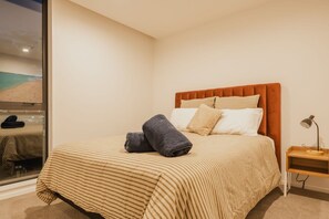 Un dormitorio con cama, almohadas, una mesita de noche y una ventana con vista al mar.