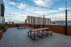 En udendørs terrasse med picnicborde og lyskæder, med udsigt over bybilledet.