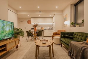 Een moderne woonkamer met een televisie, een groene bank, een eethoek met stoelen en een keuken op de achtergrond.