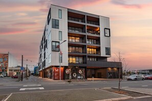 En moderne bygning med flere etager, altaner, butiksvinduer og en parkeringsplads.