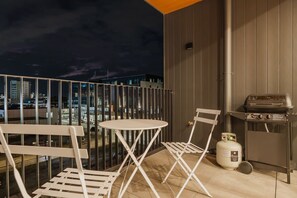 Ein Balkon mit Grill, Klappstühlen und einem Tisch.