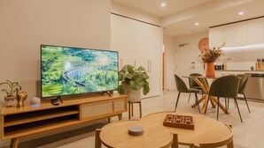 Ein modernes Wohnzimmer mit Flachbildfernseher, einem Esstisch, Stühlen und einer Küchenzeile im Hintergrund.