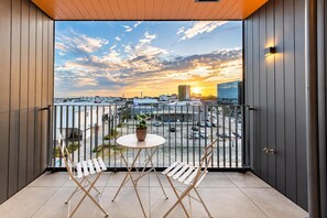 A balcony with a view of a sunset over a cityscape, featuring a table with chairs and a potted plant. - Near One NZ Stadium | 2BR | Balcony + Parking (Christchurch Central City)