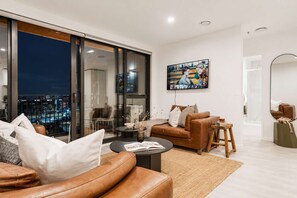 A modern living room with a large window, a flat-screen TV, and a sofa set.