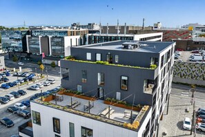 Ein modernes Gebäude mit Dachgarten, Parkplatz und angrenzenden Geschäftsgebäuden.