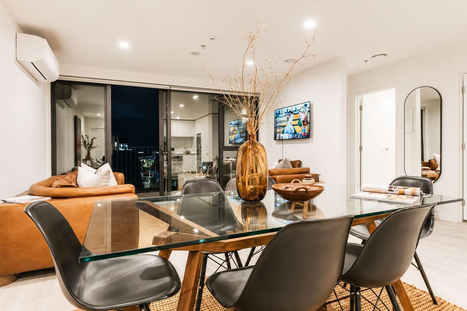 Una sala de estar moderna con una mesa de comedor de vidrio, sofás de cuero y un jarrón grande.