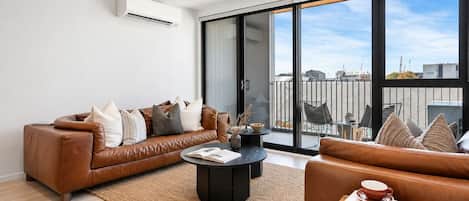 Una sala de estar moderna con un sofá de cuero marrón, una mesa de centro negra y vistas de la ciudad a través de amplios ventanales.