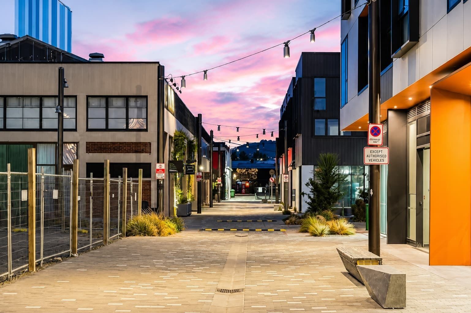 A pedestrian street lined with modern buildings, a clear sky, and a street sign indicating no parking except authorized vehicles.