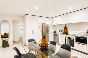 A modern kitchen with white cabinetry, a dining table with chairs, and a large vase with branches.
