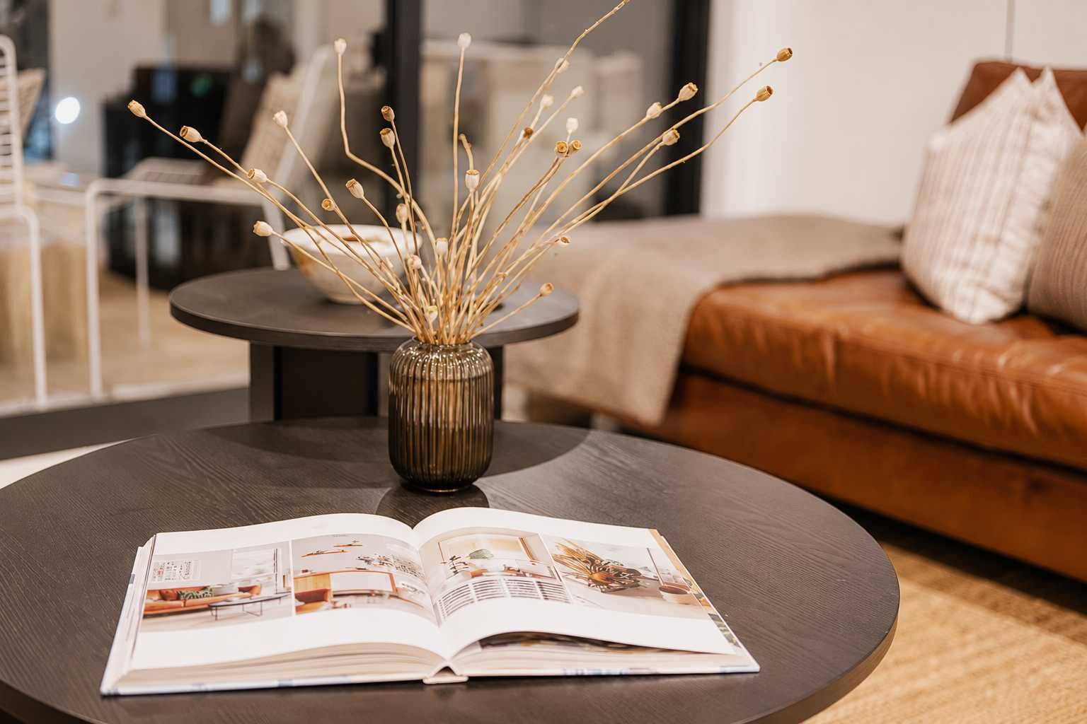 Ein modernes Wohnzimmer mit einem runden Couchtisch, einem Buch und einer Vase mit getrockneten Ästen.