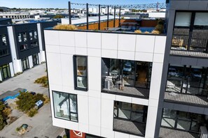 Ein modernes Gebäude mit mehreren Balkonen, großen Fenstern und einer Dachterrasse mit Sitzgelegenheiten.
