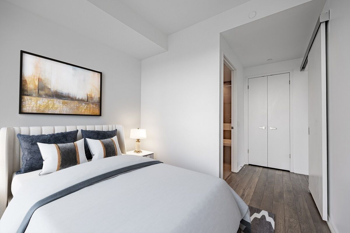 A modern bedroom with a large bed, a bedside table with a lamp, and a wardrobe.