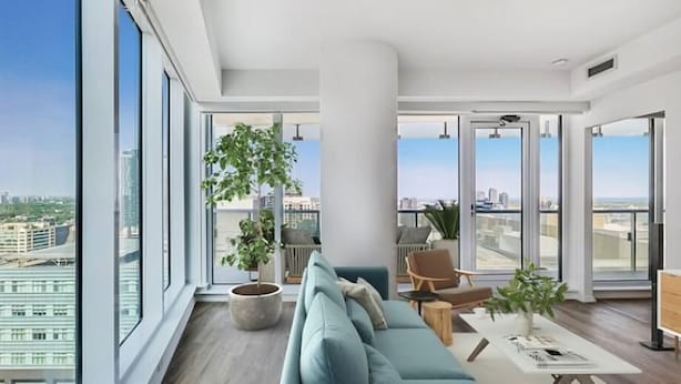 A modern living room with a large window, a sofa, a coffee table, and a potted plant. - The Mason (Toronto)