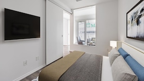 A modern hotel room with a bed, a TV, a large window, and a painting. - The Mason (Toronto)