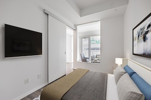 A modern hotel room with a bed, a TV, a large window, and a painting. - The Mason (Toronto)