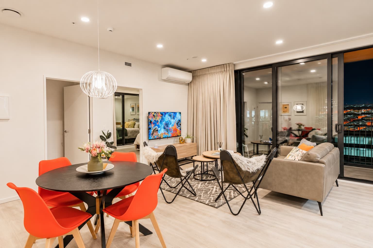A modern living room with a dining area, a sofa, a TV, and a view of a cityscape.