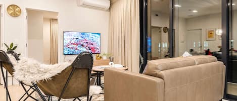 Een moderne woonkamer met een bank, een stoel, een televisie en een eethoek.