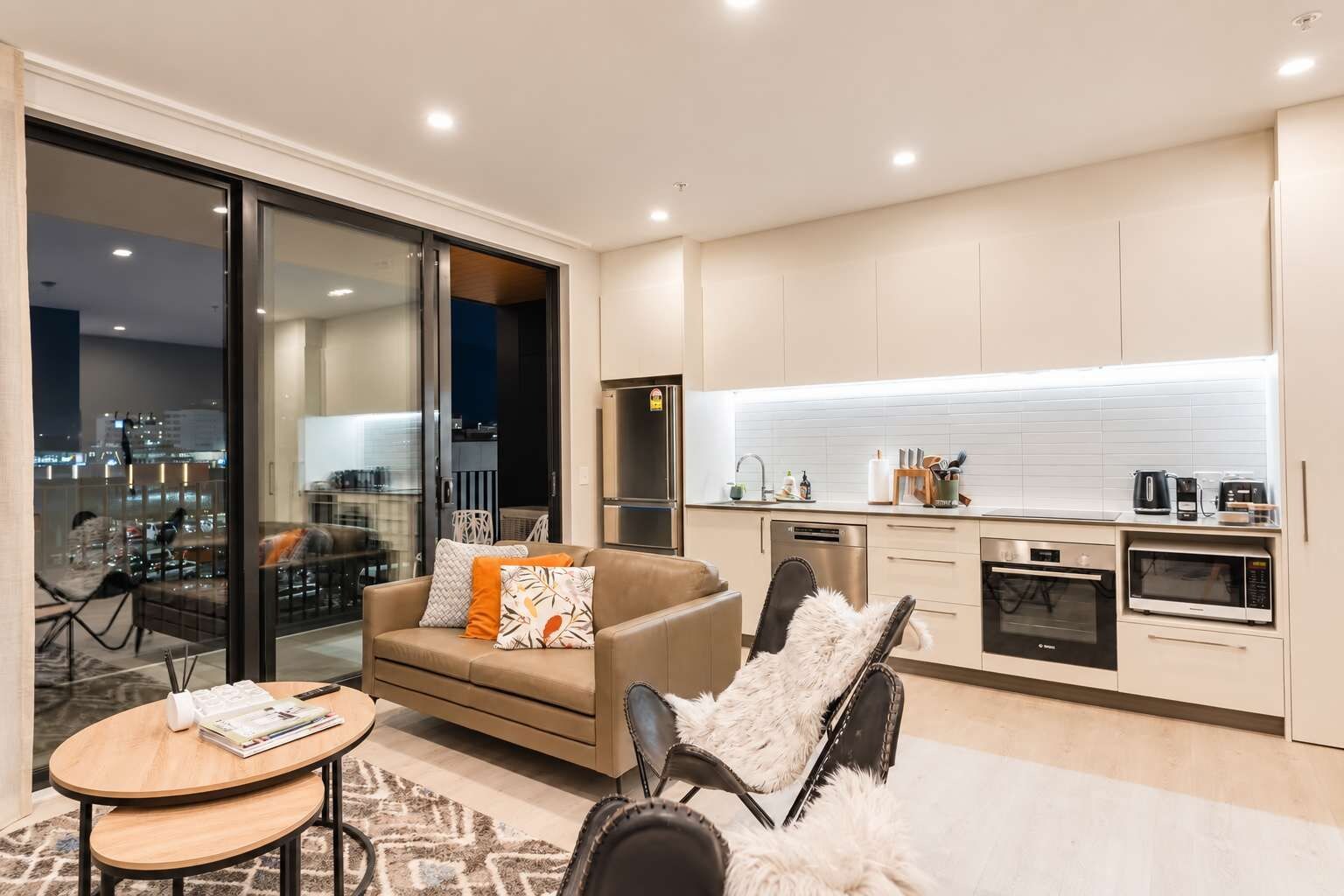 A modern apartment with a living area, kitchen, and a view of the city at night.